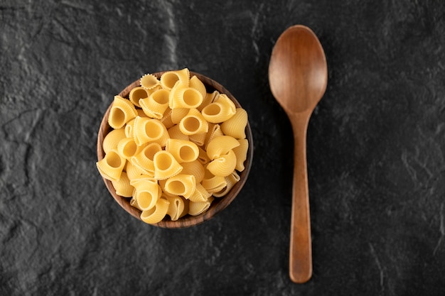 Conchiglie de pâtes italiennes non cuites dans un bol en bois avec une cuillère en bois.