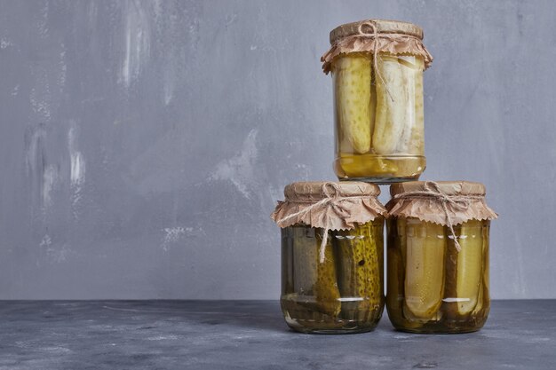 Concombres marinés dans des bocaux en verre sur fond bleu.