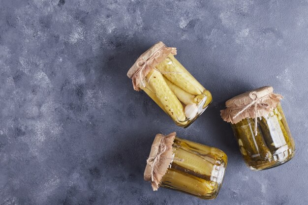 Concombres marinés dans des bocaux en verre sur fond bleu.