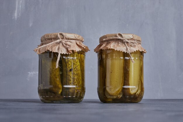 Concombres marinés dans des bocaux en verre sur fond bleu.