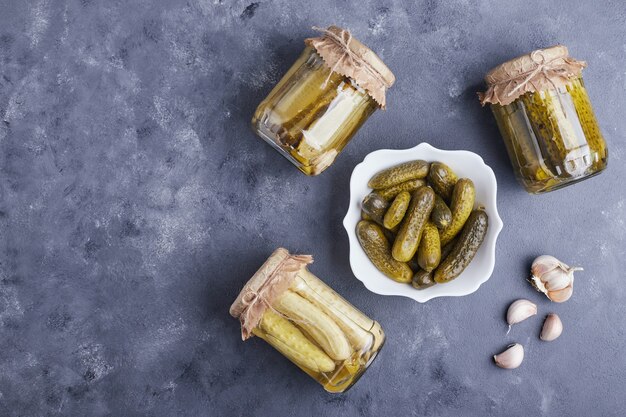 Concombres marinés dans un bol et bocaux en verre sur fond bleu avec de l'ail.