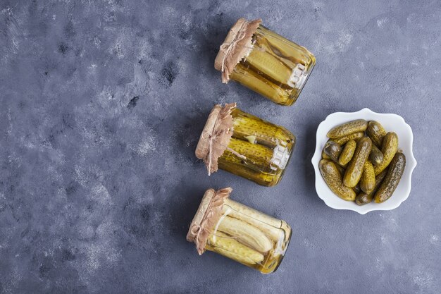 Concombres marinés dans un bol et bocaux en verre sur fond bleu.