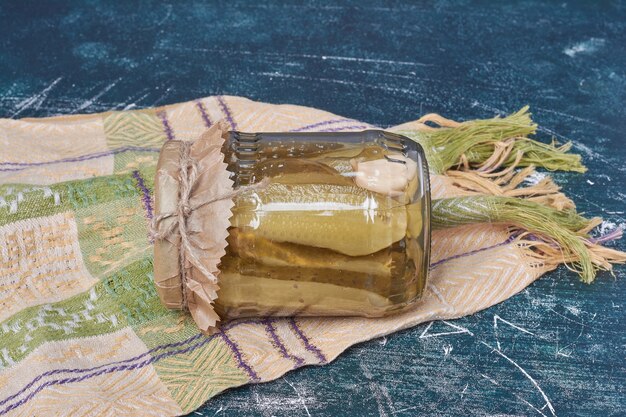 Concombres marinés maison dans un bocal en verre sur bleu avec nappe en laine.