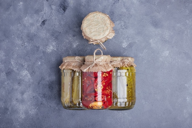 Photo gratuite concombres marinés et poivrons rouges dans des bocaux en verre sur fond bleu.