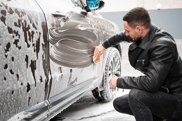 Conducteur lavant sa voiture à l'éponge avec une solution savonneuse