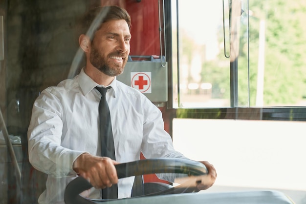 Photo gratuite un conducteur masculin joyeux regardant vers l'avant tout en conduisant les transports publics lors d'une journée chaude et ensoleillée, vue de face de