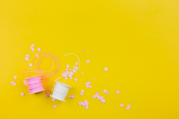 Photo gratuite confetti en papier avec une bobine rose et blanche sur fond jaune