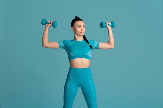 Confiance. Belle jeune athlète féminine pratiquant, portrait bleu monochrome. Modèle brune de coupe sportive avec des poids. Musculation, mode de vie sain, concept de beauté et d'action.