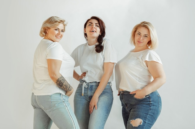 Confiance. jeunes femmes caucasiennes en vêtements décontractés s'amusant ensemble. amis posant sur fond blanc, riant, a l'air heureux, bien entretenu. bodypositive, féminisme, s'aimer soi-même, concept de beauté.