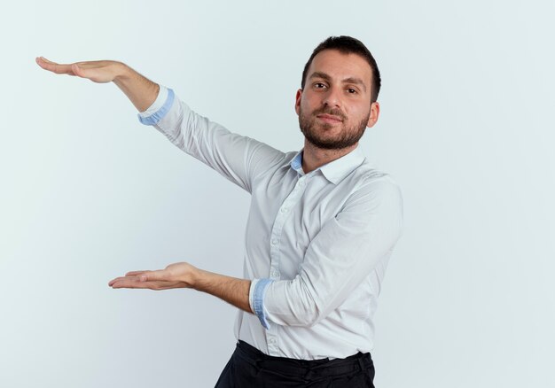 Confiant bel homme fait semblant de tenir quelque chose d'isolé sur un mur blanc