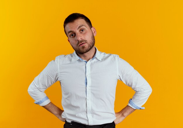 Confiant bel homme met les mains sur la taille isolé sur un mur orange