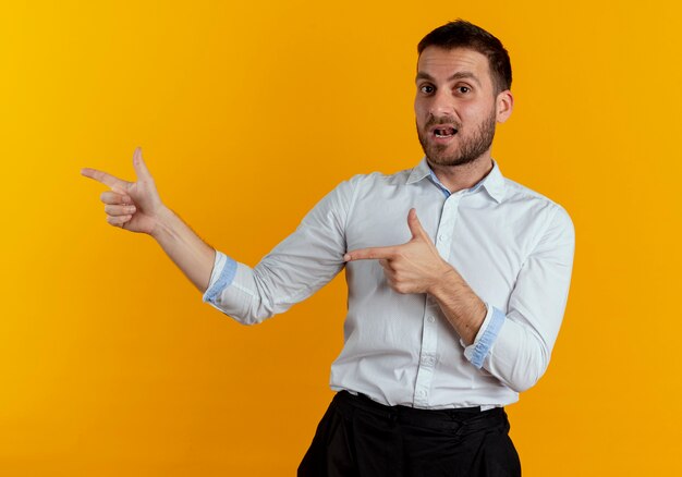 Confiant bel homme pointe sur le côté avec deux mains isolé sur un mur orange