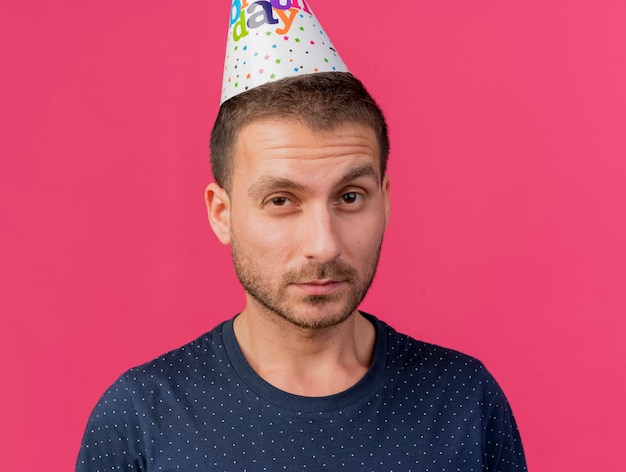 Confiant bel homme portant une casquette d'anniversaire à l'avant isolé sur un mur rose