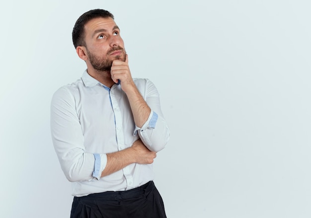 Confiant bel homme tient le menton et lève les yeux isolé sur un mur blanc