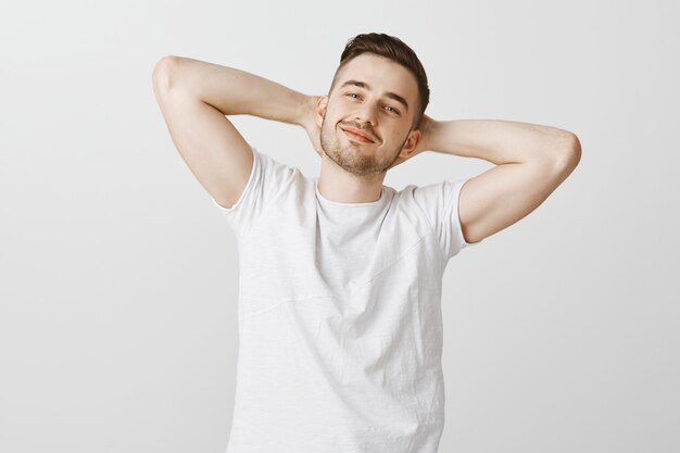 Confiant heureux bel homme tenant les mains derrière la tête et souriant heureux