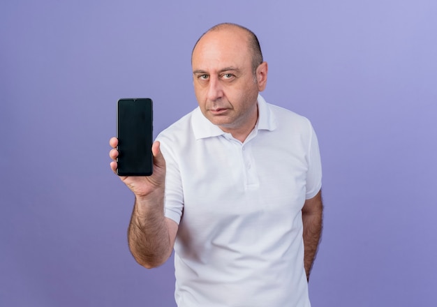 Confiant homme d'affaires mature occasionnel montrant un téléphone mobile regardant la caméra isolée sur fond violet avec espace de copie