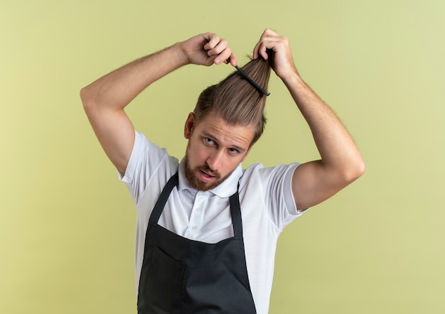 Confiant jeune beau coiffeur peignant ses cheveux à côté isolé sur vert olive