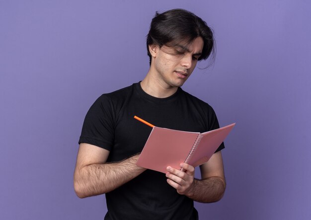 Confiant jeune beau mec portant un t-shirt noir écrit quelque chose sur un ordinateur portable isolé sur un mur violet