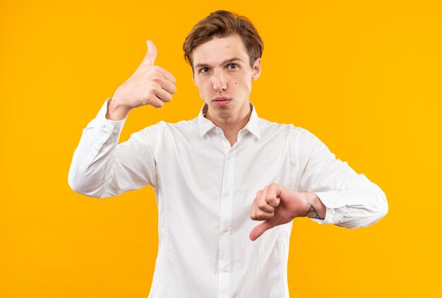 Confiant jeune beau mec vêtu d'une chemise blanche montrant les pouces de haut en bas