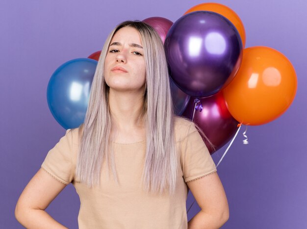 Confiant jeune belle fille debout devant des ballons isolés sur mur bleu