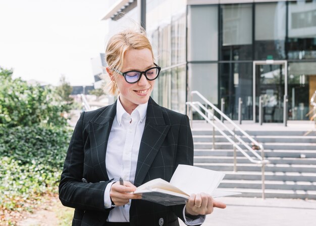 Confiant, jeune femme affaires, debout, dehors, bureau, regarder, journal