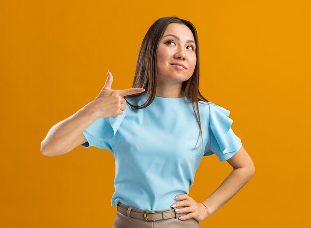 Confiant jeune femme asiatique levant le côté pointé isolé sur mur orange