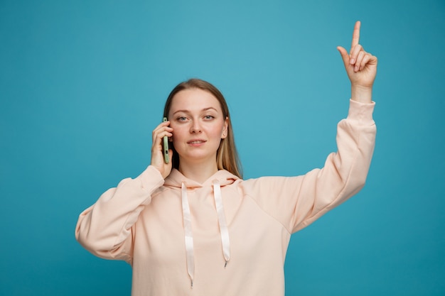 Confiant jeune femme blonde parlant au téléphone pointant vers le haut