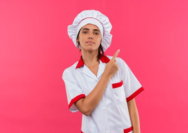 Confiant jeune femme cuisinier portant des points uniformes de chef à côté sur un mur rose isolé avec copie espace