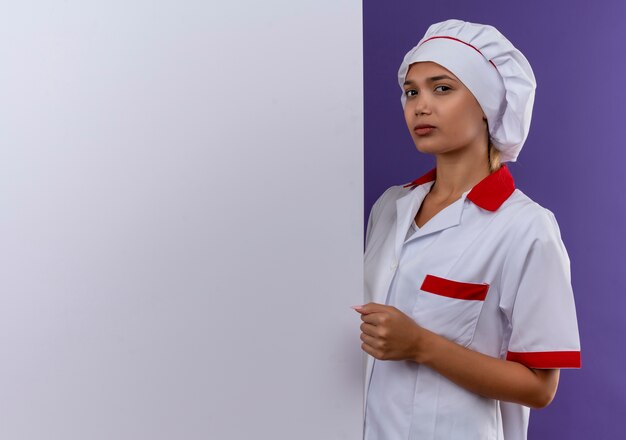 Confiant jeune femme cuisinier portant l'uniforme de chef tenant un mur blanc sur un mur isolé avec copie espace