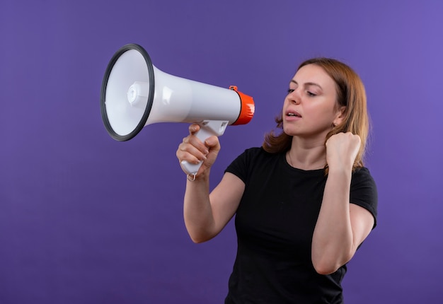 Confiant jeune femme décontractée parlant par le haut-parleur avec le poing levé sur l'espace violet isolé