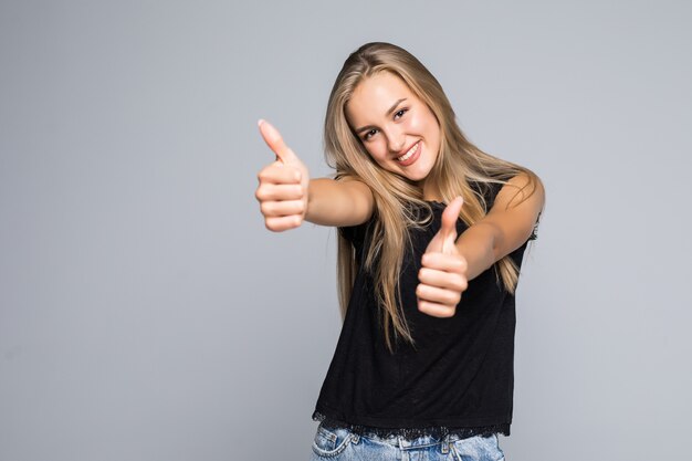 Confiant jeune femme donnant les pouces vers le haut sur un fond gris