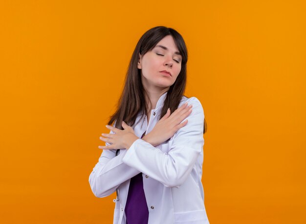 Confiant jeune femme médecin en robe médicale avec stéthoscope croise les bras et met les mains sur les épaules sur fond orange isolé avec copie espace