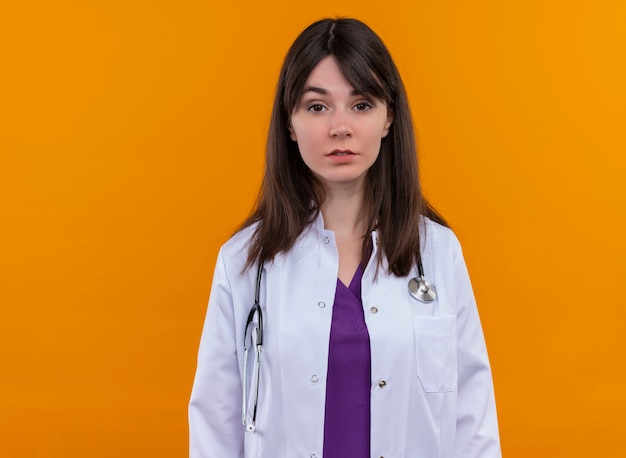 Confiant jeune femme médecin en robe médicale avec stéthoscope regarde la caméra sur fond orange isolé avec copie espace