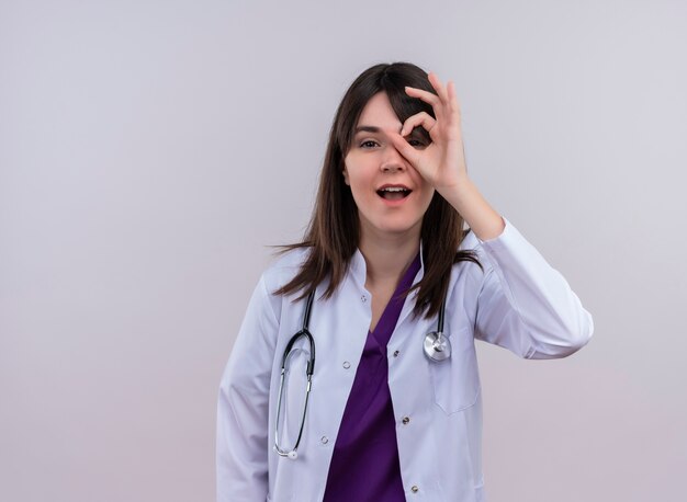 Confiant jeune femme médecin en robe médicale avec stéthoscope regarde le geste sur fond blanc isolé avec copie espace