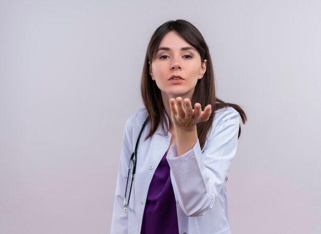 Confiant jeune femme médecin en robe médicale avec stéthoscope tient la main ouverte et regarde la caméra sur fond blanc isolé avec copie espace