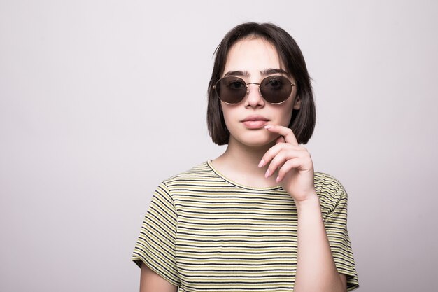 Confiant jeune femme regardant à travers des lunettes de soleil isolées