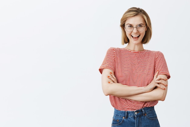 Confiant jeune femme souriante à lunettes croiser la poitrine des bras et à la recherche impertinente