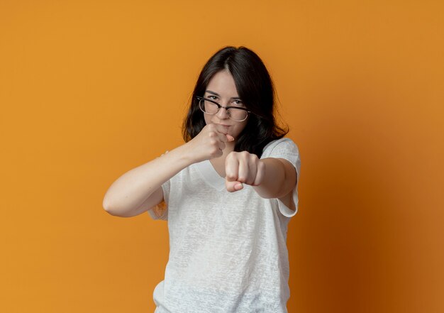 Confiant jeune fille assez caucasienne portant des lunettes faisant le geste de boxe à la caméra isolée sur fond orange avec espace de copie