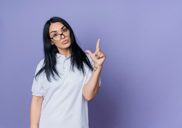 Confiant jeune fille brune caucasienne à lunettes optiques pointe vers le haut isolé sur mur violet