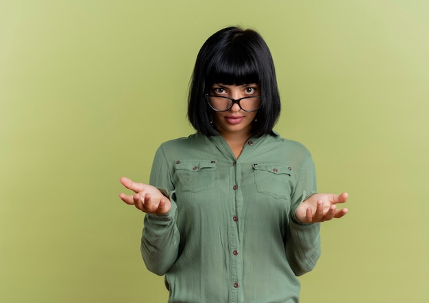 Photo gratuite confiant jeune fille brune caucasienne à lunettes optiques tient les mains ouvertes à la recherche