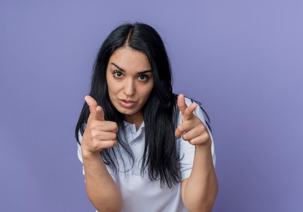 Confiant jeune fille brune caucasienne points avec deux mains isolés sur un mur violet