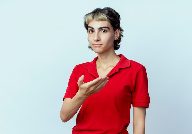 Confiant jeune fille de race blanche avec coupe de cheveux de lutin montrant la main vide isolé sur fond blanc avec espace de copie