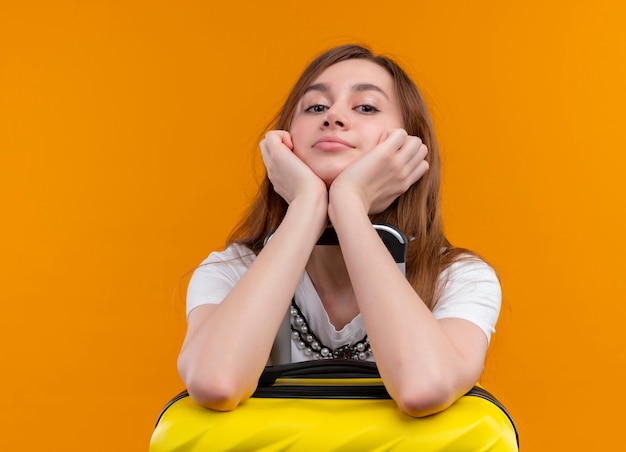 Confiant jeune fille de voyageur mettant les bras sur la valise sur un espace orange isolé avec copie espace