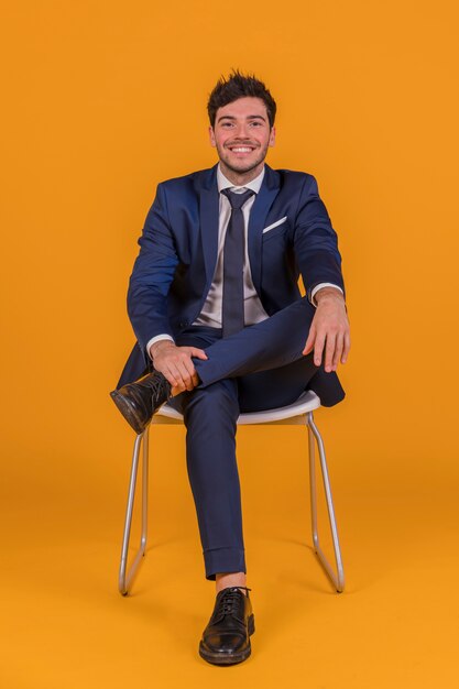 Confiant jeune homme d&#39;affaires assis sur une chaise blanche sur un fond orange
