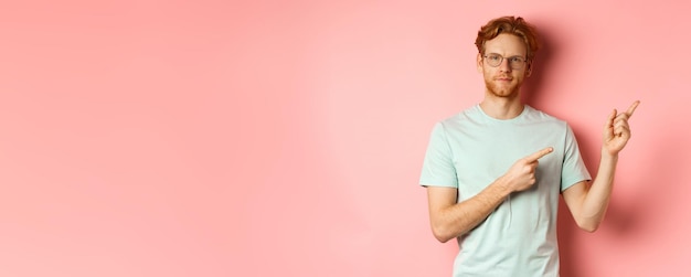 Photo gratuite confiant jeune homme aux cheveux roux et à la barbe souriant heureux et pointant du doigt le coin supérieur droit c