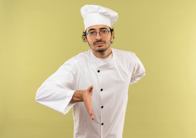 Confiant jeune homme cuisinier portant l'uniforme de chef et des lunettes tenant la main