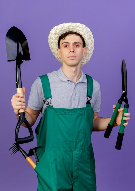 Confiant Jeune Homme Jardinier Portant Chapeau De Jardinage Se Dresse Avec Des Outils De Jardinage