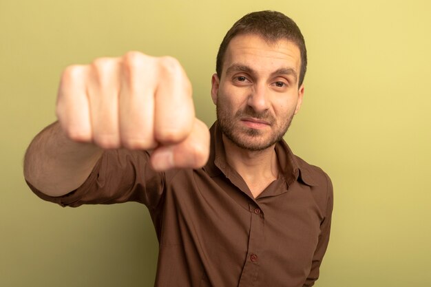 Confiant jeune homme de race blanche regardant la caméra étirant le poing vers la caméra isolée sur fond vert olive