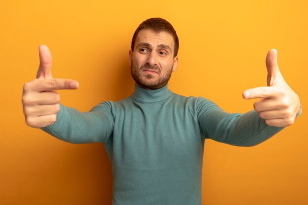 Confiant jeune homme regardant côté pointant vers l'espace en face de lui isolé sur mur orange