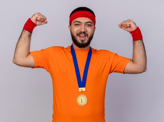 Confiant jeune homme sportif portant bandeau et bracelet avec médaille montrant un geste fort isolé sur fond blanc